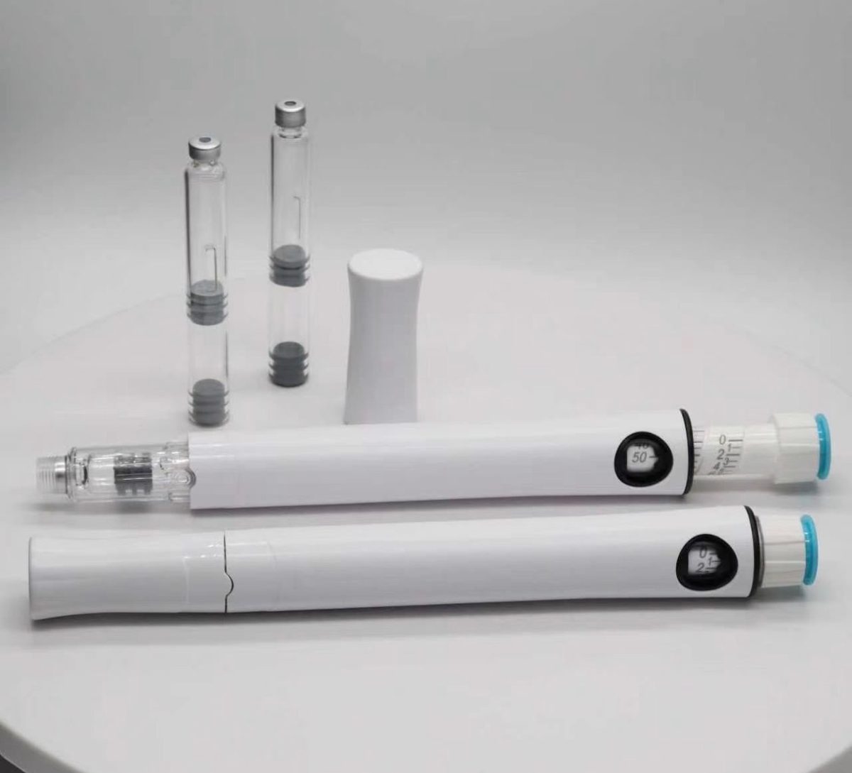 Two white multi-dose pen injectors with dose windows, a pen cap and two glass cartridges